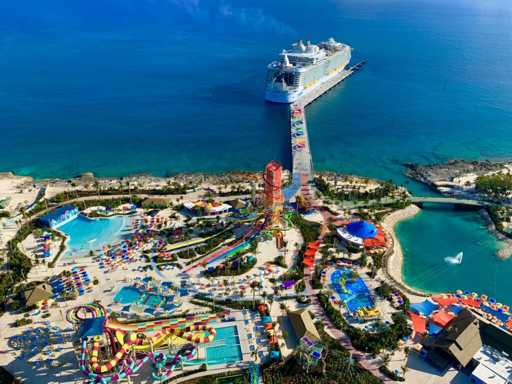 Vista de cima de um destino de ilha privada da Royal Caribbean, Perfect Day at CocoCay. Um navio está atracado no píer, e a ilha é preenchida com várias piscinas, escorregadores aquáticos e áreas de lazer coloridas, cercadas por águas azuis claras.