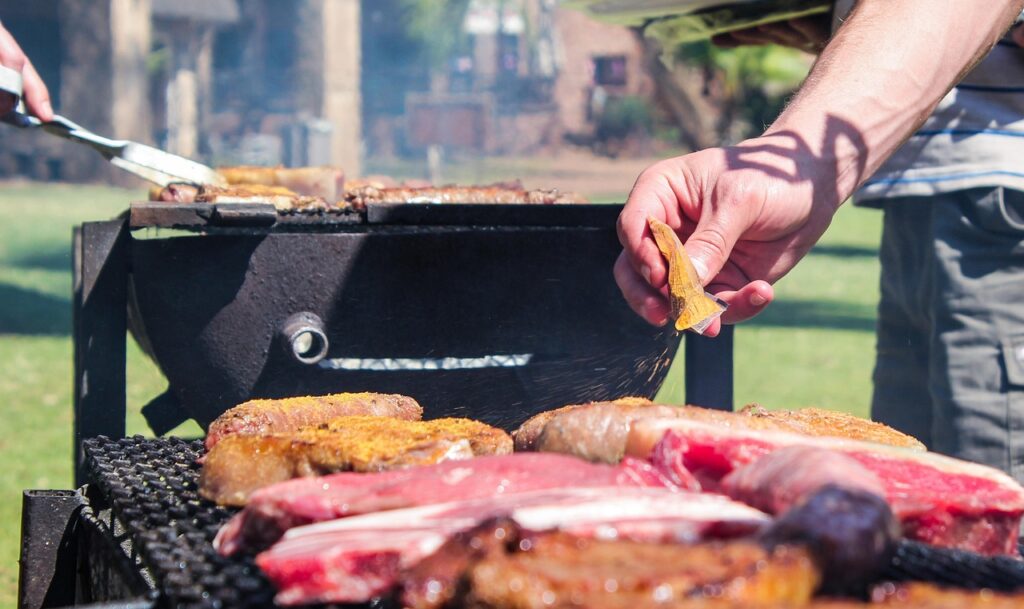 A imagem vibrante mostra um autêntico "braai" sul-africano, com carnes e linguiças grelhando sobre as brasas