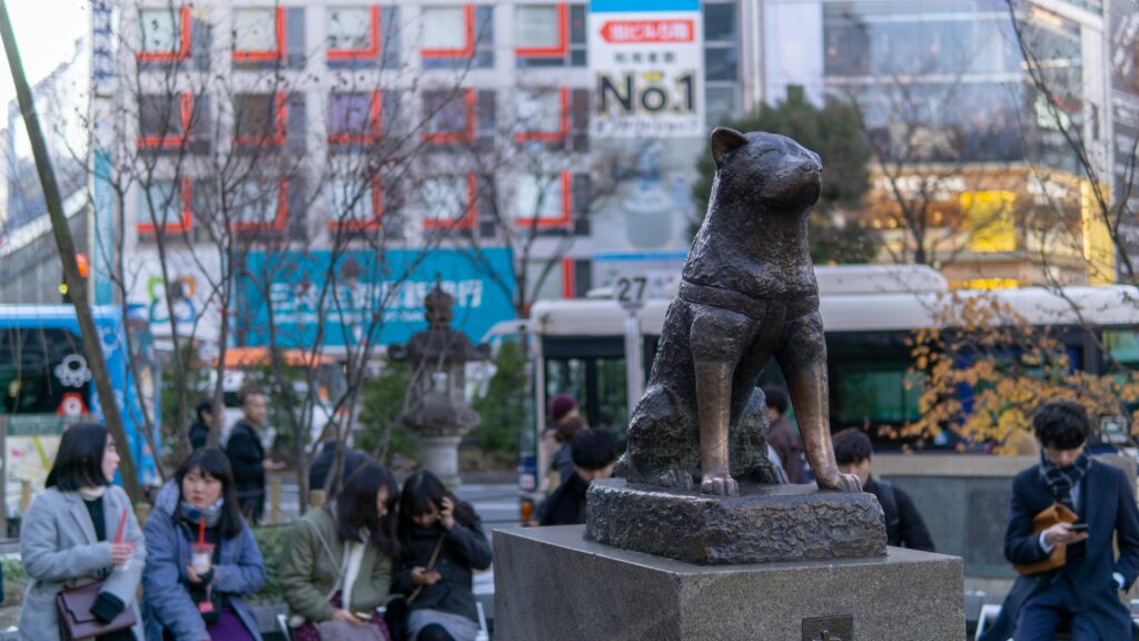 Estátua do cachorro Hachiko em frente à estação de Shibuya, Tóquio, Japão, com pessoas ao redor.