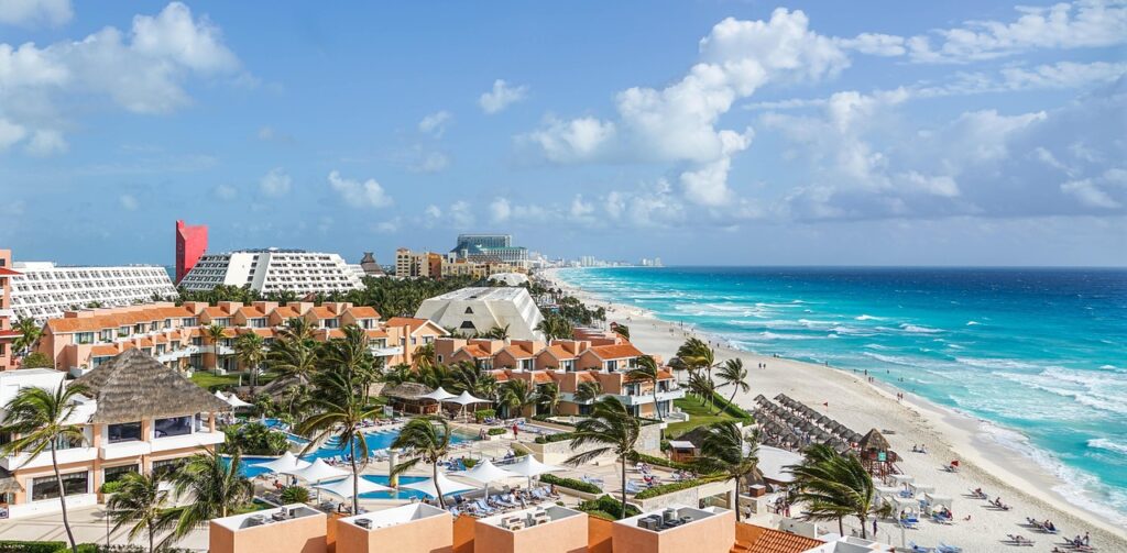 A imagem mostra a famosa faixa de hotéis e resorts de Cancún, no México, com praias de areia fina, águas azul-turquesa e céu ensolarado — cenário perfeito para quem busca um destino de férias no Caribe. Palavras-chave: Cancún, Zona Hotelera, resorts all-inclusive, praia de areia branca, mar do Caribe, viagem ao México.