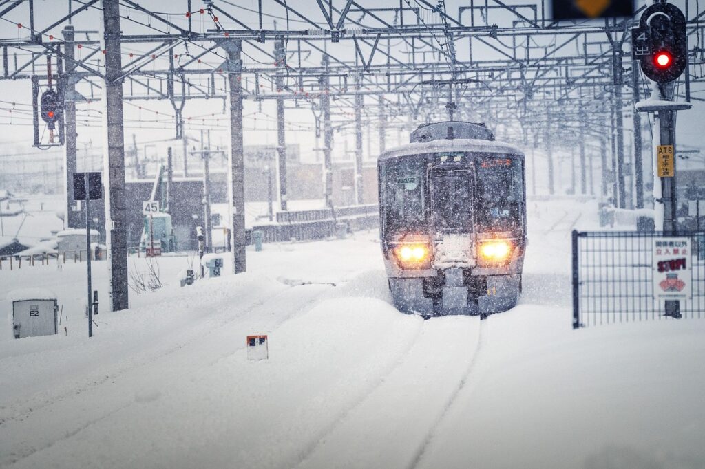 Trem no Japão coberto de neve em uma estação ferroviária durante uma nevasca, com trilhos e paisagem nevada.