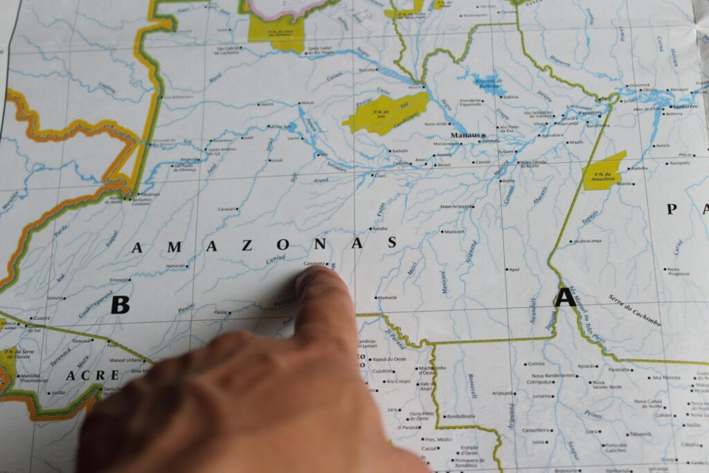 Mão apontando para o estado do Amazonas em um mapa do Brasil, com a cidade de Manaus claramente visível, indicando o destino de viagem na Amazônia.