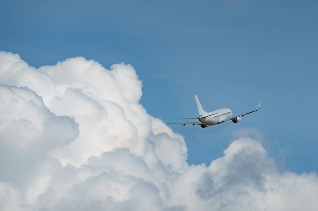 vião a jato branco em ascensão no céu azul, com grandes nuvens brancas e volumosas ao redor. A imagem sugere viagem e chegada a um destino de férias, como Jericoacoara.